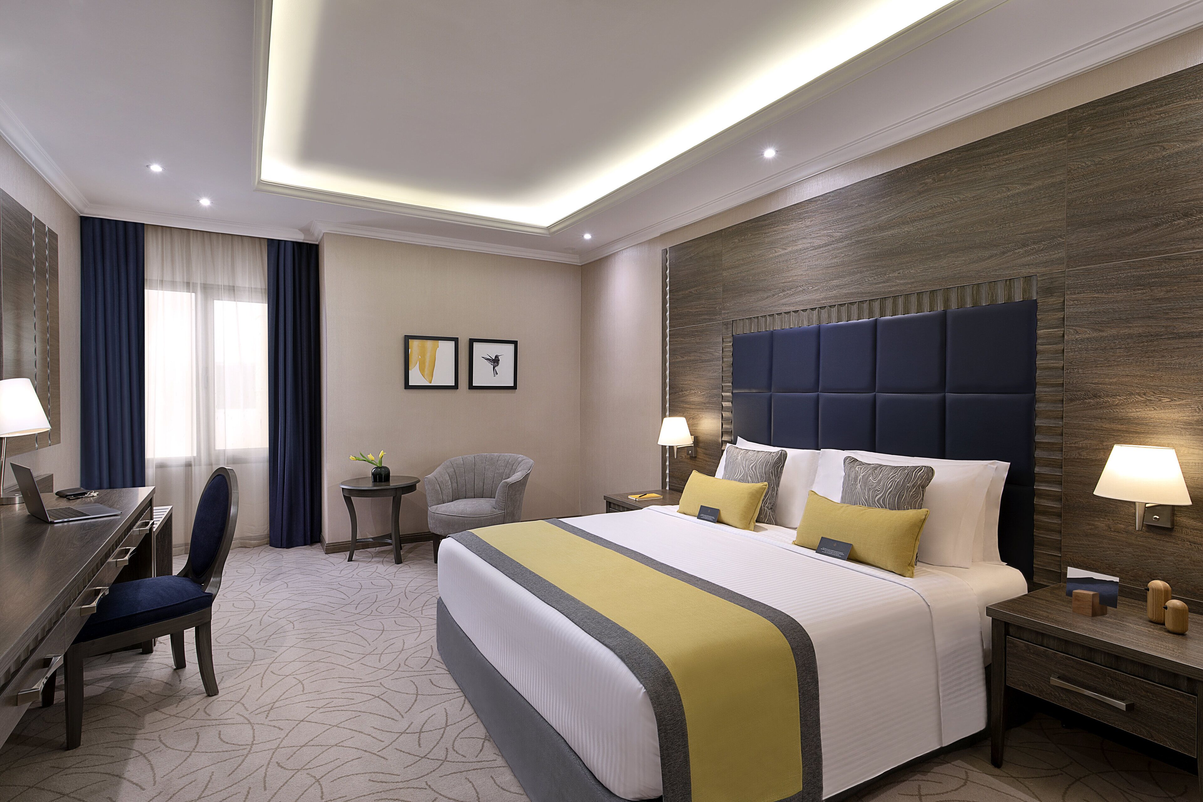 A hotel room with a large bed, a desk, a chair, a nightstand, and a lamp.
