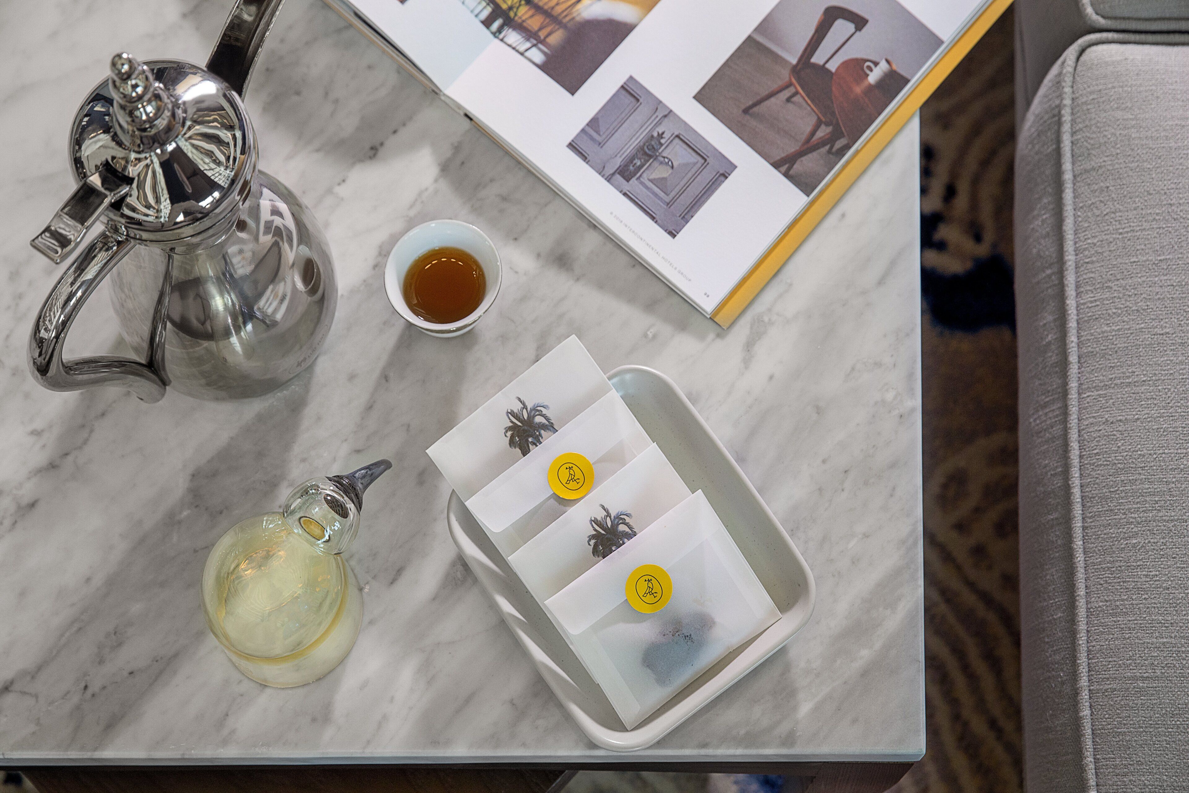 Une table en marbre, une théière en argent, un petit bol de thé et un plateau avec des sachets de thé.