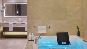 A modern bathroom with a large mirror, a sink with toiletries, and a bathtub with a control panel.