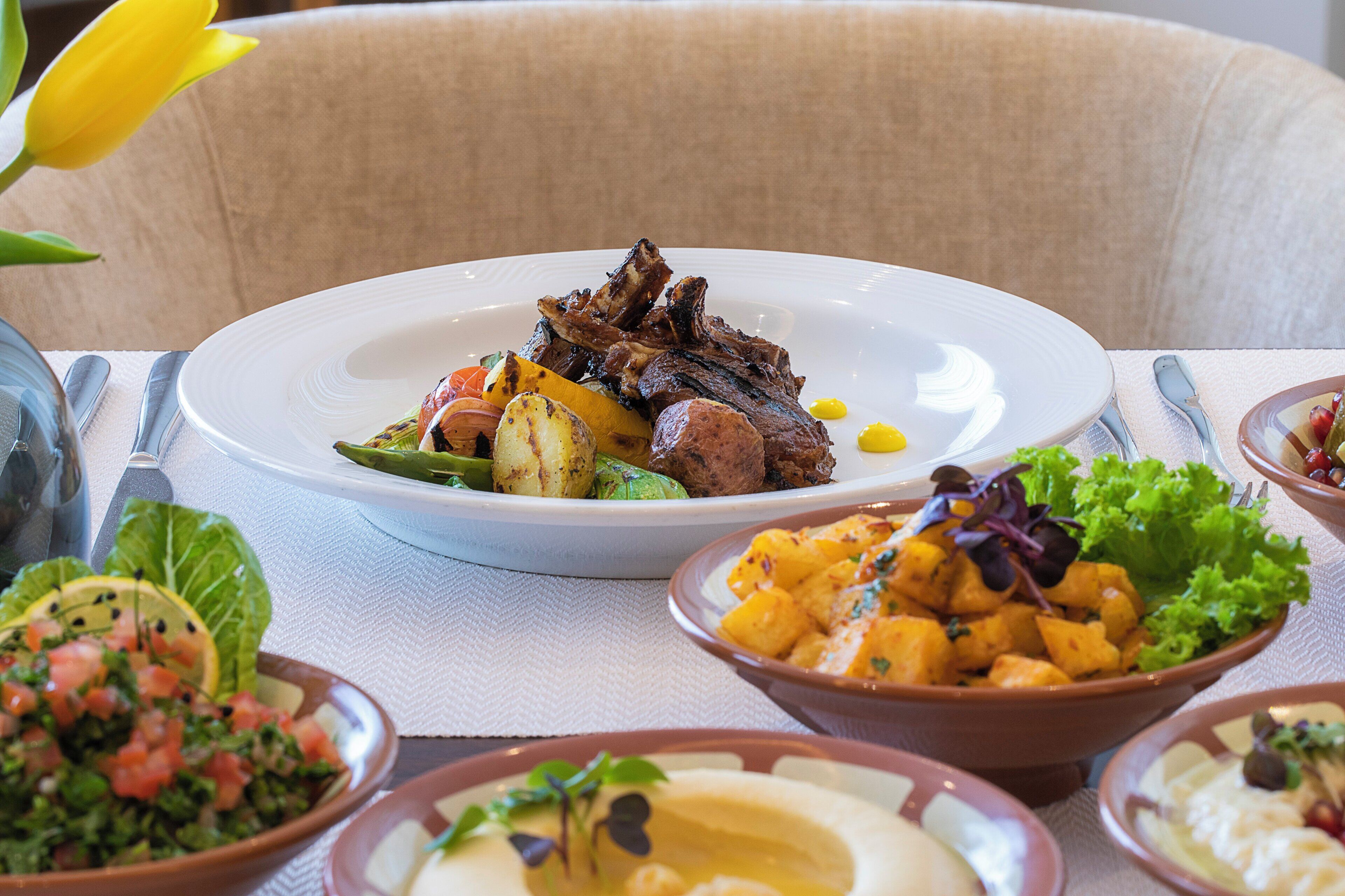 A dining table with a plate of food, including grilled meat and vegetables, and several side dishes.