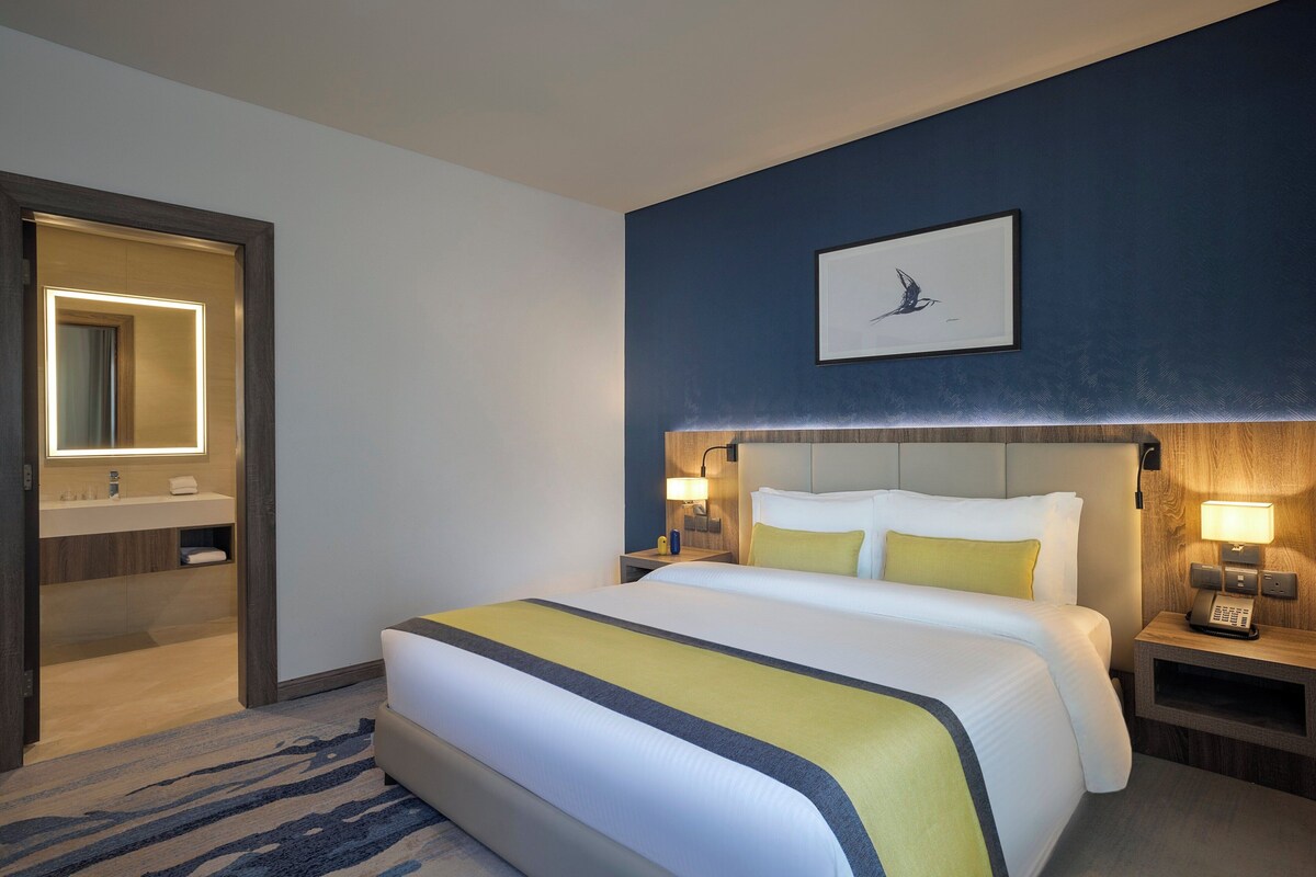 A hotel room with a large bed, bedside tables with lamps, a mirror, and a framed picture on the wall.