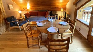 A cozy dining area with a wooden table set for four, surrounded by wooden chairs. A sofa and a chair are positioned against the wall, with a lamp on a side table. - Renovated 2-room apartment, 5 people, Méribel Altiport, ski-in/ski-out (Méribel)