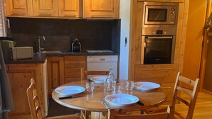 A wooden dining table with plates and glasses, surrounded by wooden chairs, in a kitchen with wooden cabinets and appliances. - Renovated 2-room apartment, 5 people, Méribel Altiport, ski-in/ski-out (Méribel)