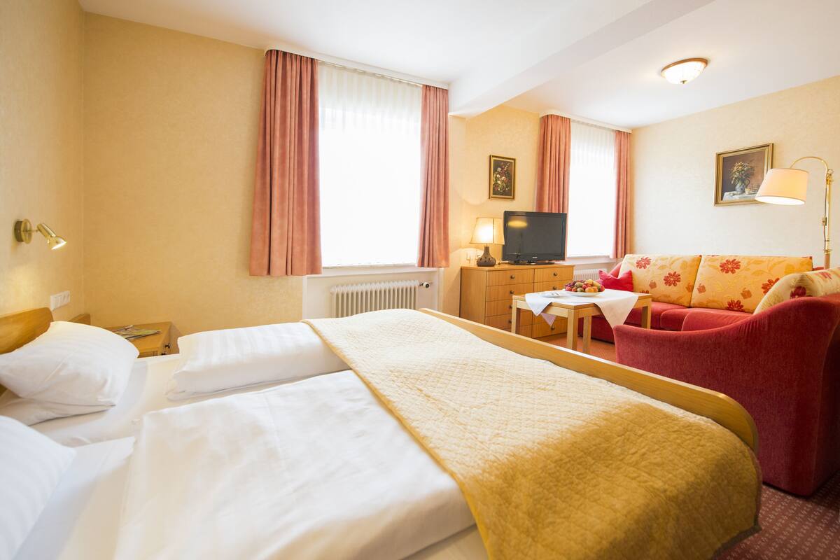 Una habitación de hotel con cama, sofá, televisión y lámpara.