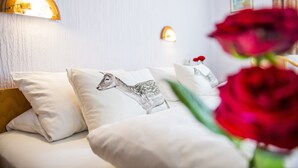 A bed with white bedding and a pillow with a deer design, a wall-mounted light fixture, and a red rose in the foreground. - Hotel Gasthof Jägerstüble (Freudenstadt)