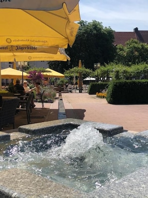 An outdoor seating area with yellow umbrellas, a water feature, and a paved walkway.