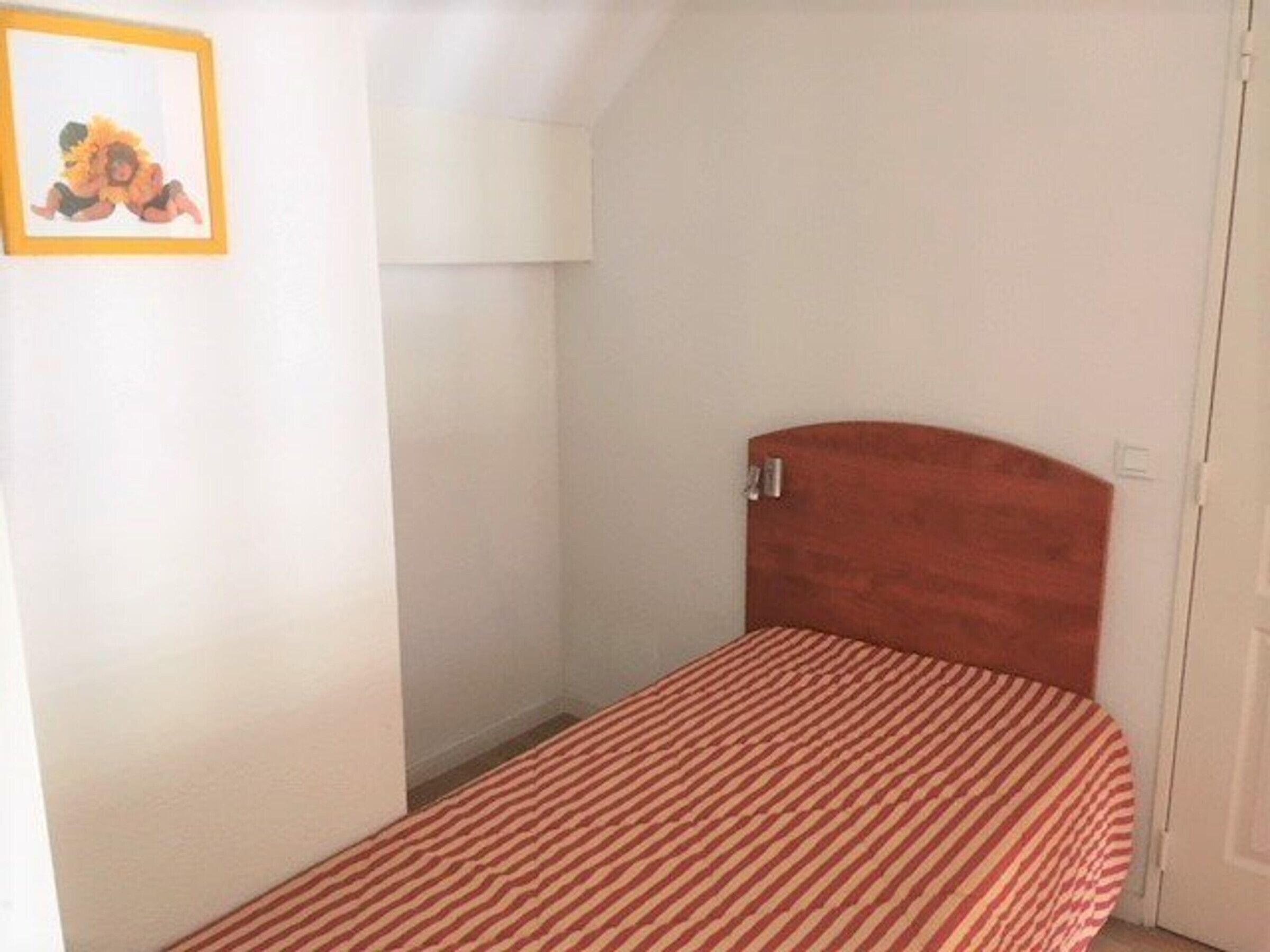A small, single-bed room with a striped bedspread, a wooden headboard, and a framed picture on the wall.
