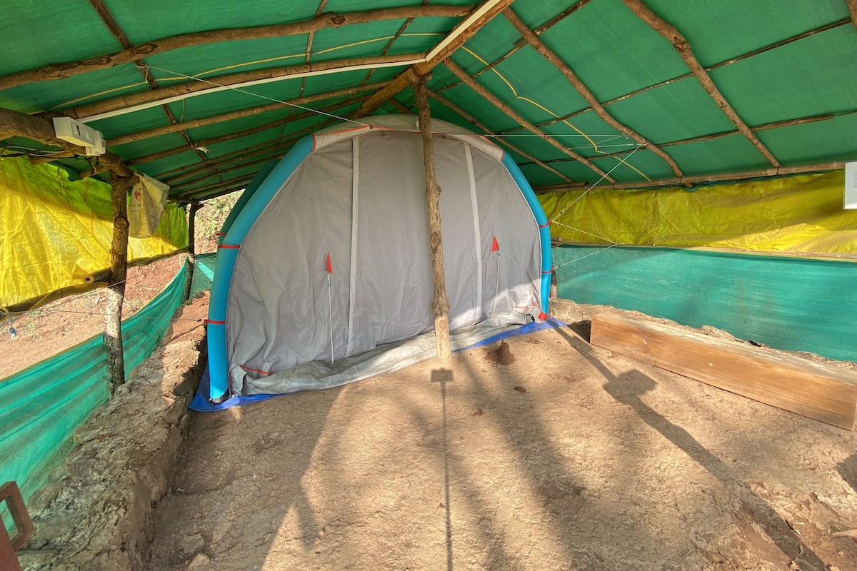 A tent with a green roof and grey walls, surrounded by green and yellow tarps.