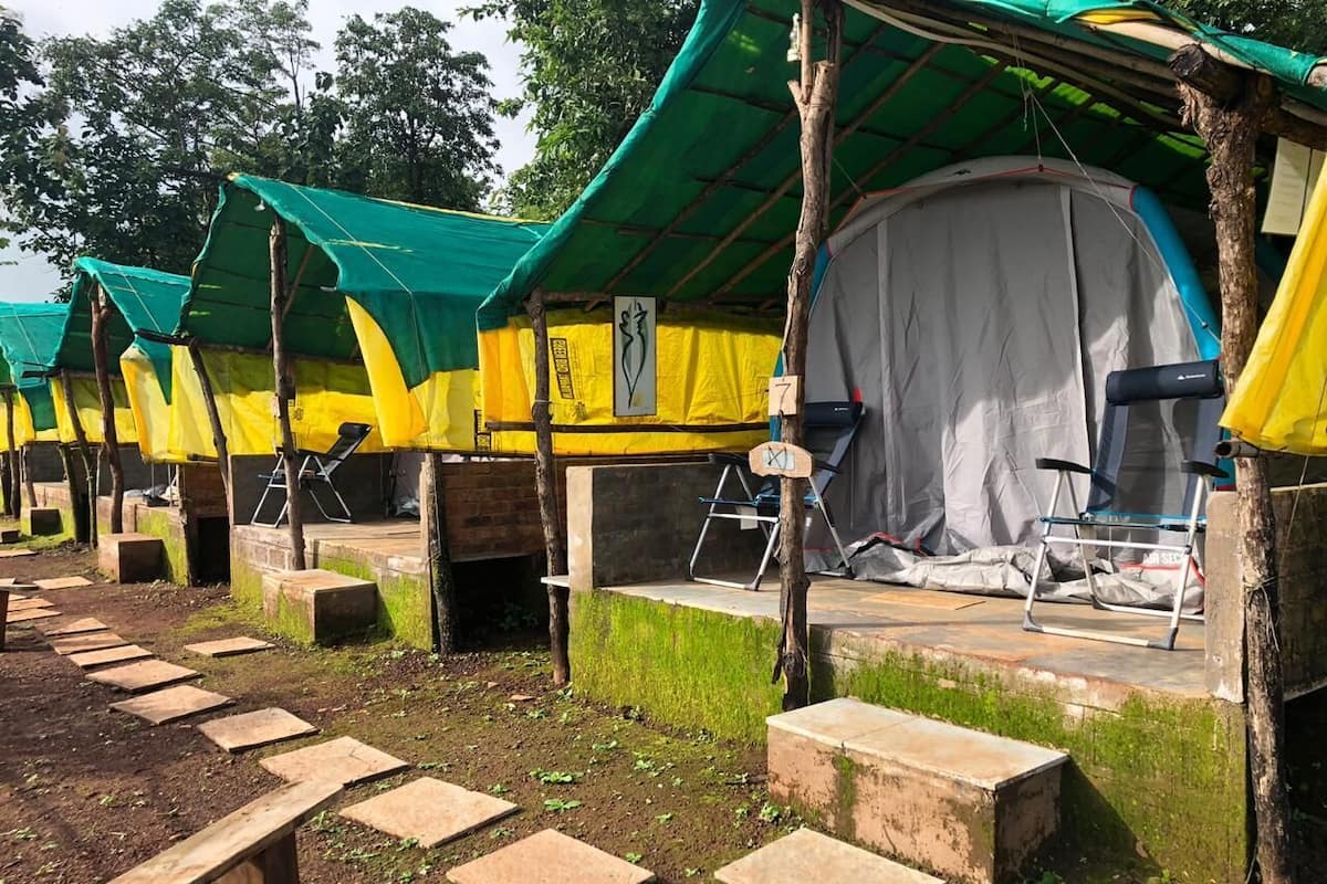 A row of tents with green and yellow canopies, some with white curtains, and a grey tent with a black chair.