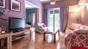 A living room with a TV, a sofa, a coffee table, and a patterned bedspread. - S&K Polyxene Suite in Center of Athens (Athens)