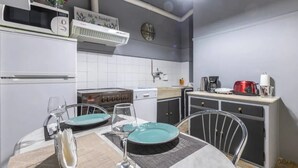 A compact kitchen with white appliances, a dining table with two chairs, and a clock on the wall. - S&K Polyxene Suite in Center of Athens (Athens)