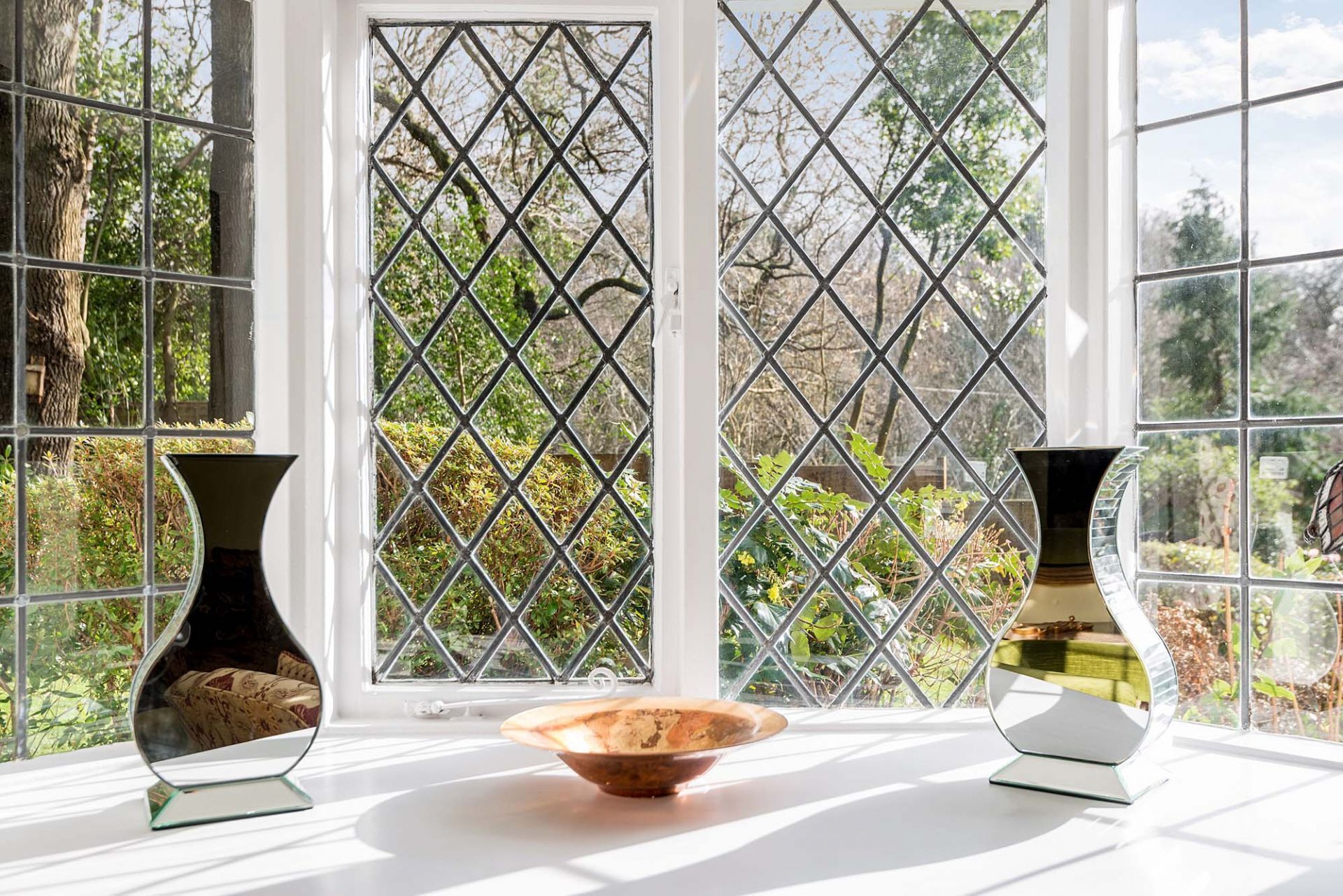 Une pièce dotée d’une grande fenêtre ornée d’une grille à motifs losangés, de deux vases posés sur une surface blanche et d’un bol placé au centre.