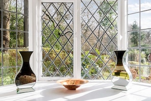 A room with a large window featuring a diamond-patterned grille, two vases on a white surface, and a bowl in the center.