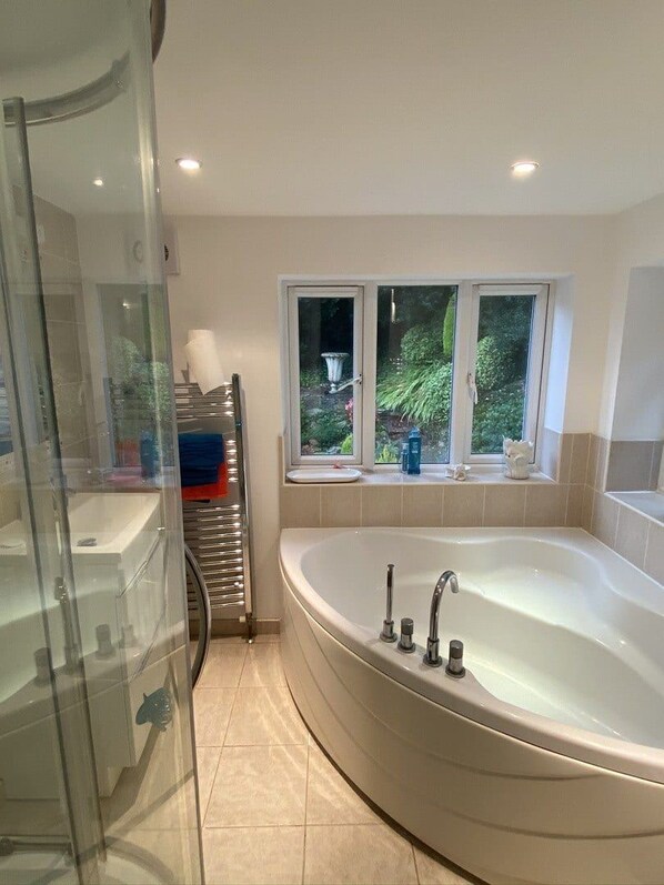 A bathroom with a bathtub, a glass shower enclosure, and a window with a view of greenery.