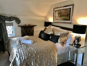 A neatly arranged bedroom with a bed, bedside tables, a nightstand, a framed picture on the wall, and a window with curtains.