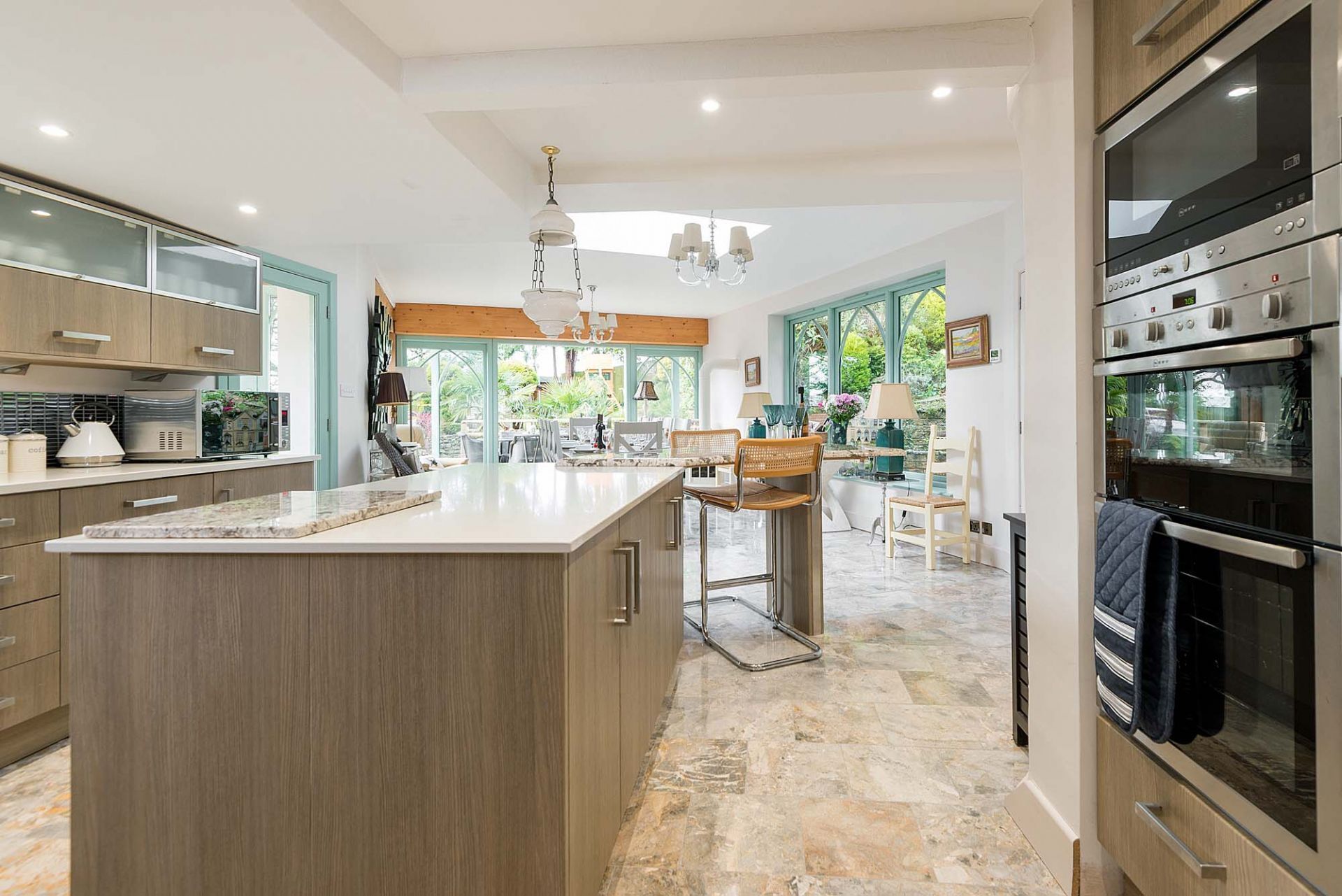 A modern kitchen with a large island, stainless steel appliances, and a view of the garden.