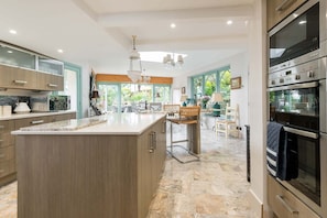 Une cuisine moderne dotée d’un grand îlot central, d’appareils électroménagers en acier inoxydable et offrant une vue sur le jardin.