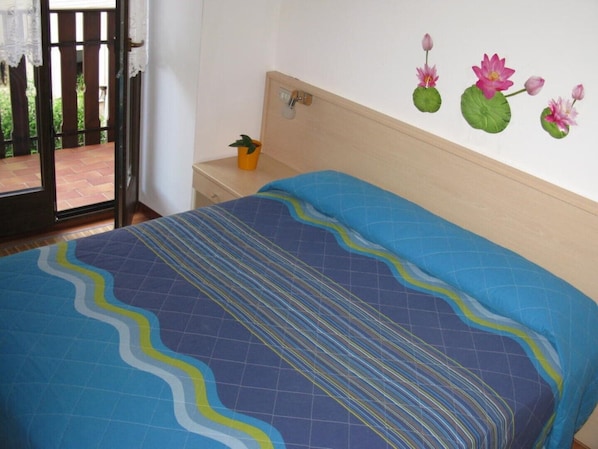 A bedroom with a bed, a nightstand, a potted plant, and a wall with a floral decoration.