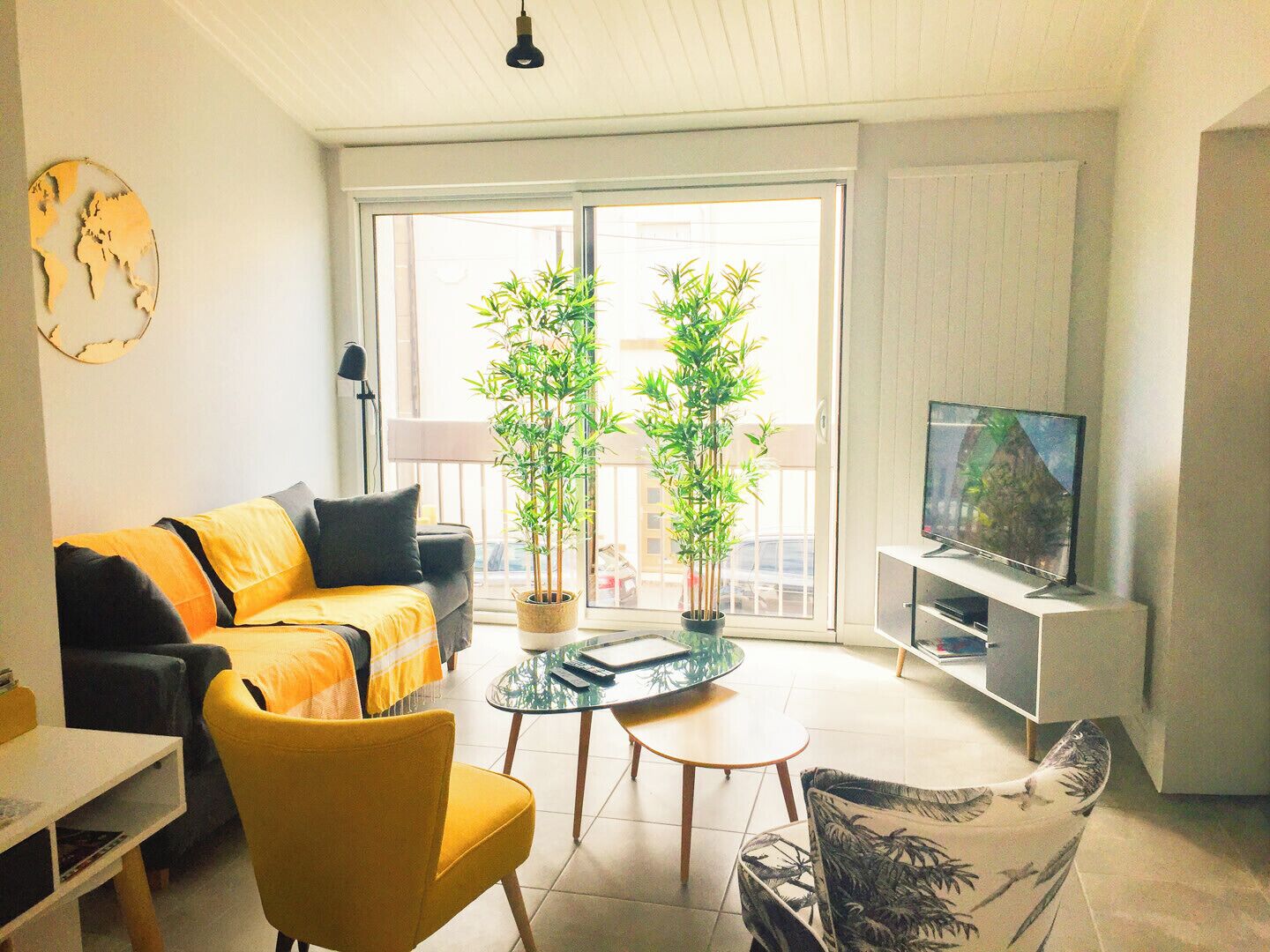 Un salon avec un canapé, des fauteuils, un téléviseur et deux plantes en pot.