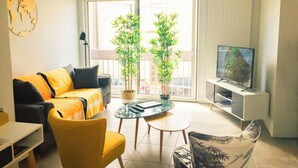 A living room with a sofa, chairs, a TV, and two potted plants. - Beautiful renovated townhouse in the heart of Arago (Les Sables-d'Olonne)