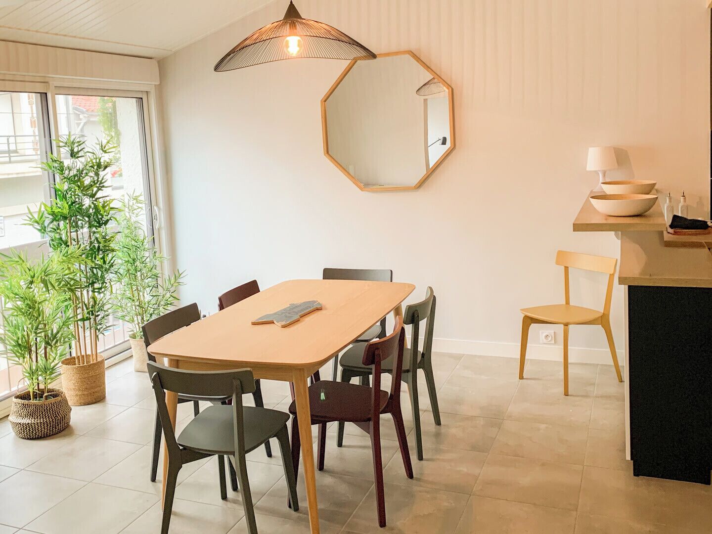 Un coin repas avec une table en bois, des chaises, un miroir hexagonal et des plantes en pot.