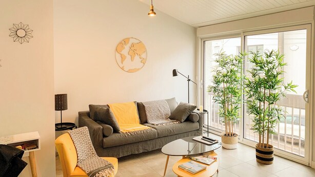 A modern living room with a sofa, a coffee table, a lamp, and two potted plants. - Beautiful renovated townhouse in the heart of Arago (Les Sables-d'Olonne)