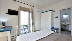 A hotel room with a bed, a desk with a chair, a wardrobe, a bathroom with a sink, and a television on the wall. - INAH Boutique Rooms (Dorgali)