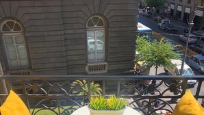 A balcony with a small table and two chairs, a potted plant, and a view of a street with buildings and parked cars. - Umberto34 - Luxury Home (Naples)