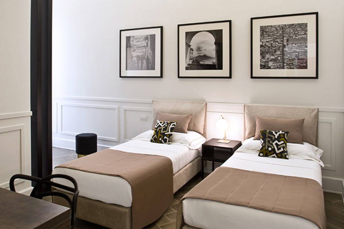 A hotel room with two beds, a table, and three framed pictures on the wall.
