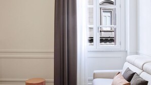 A room with a herringbone floor, a white sofa with cushions, a pink ottoman, and a window with curtains. - Umberto34 - Luxury Home (Naples)