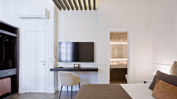 A modern hotel room with a bed, a desk with a flat-screen TV, a chair, and a walk-in closet. - Umberto34 - Luxury Home (Naples)