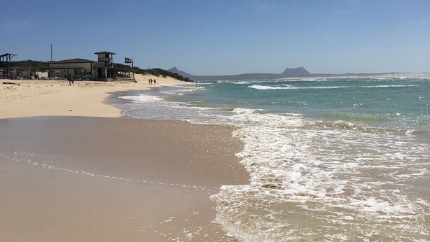 Ein Strand mit einem Rettungsturm, sandigem Ufer und blauem Himmel.