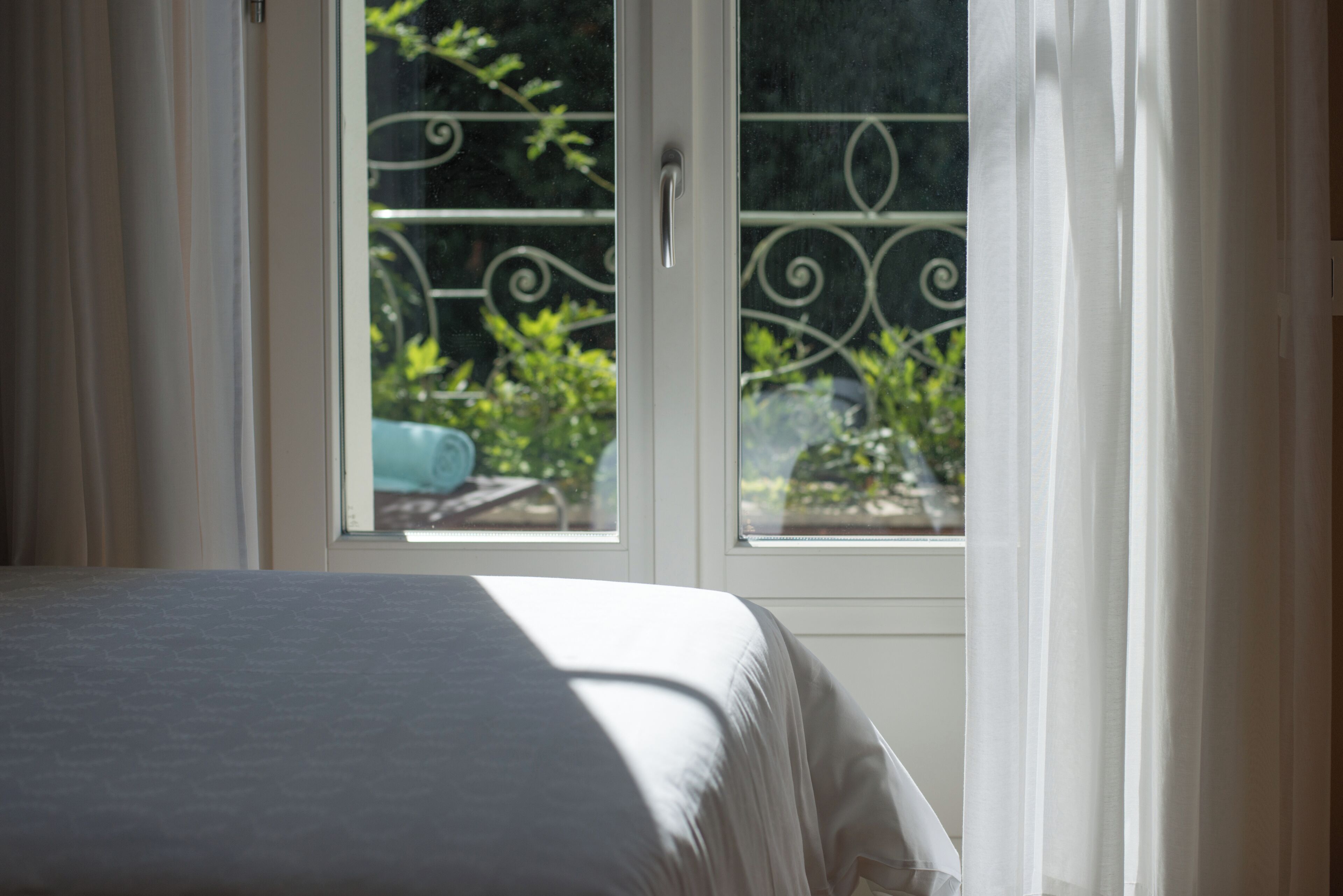 A bedroom with a bed, a window with curtains, and a view of greenery outside.