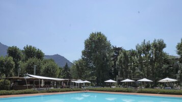 A pool area with lounge chairs and umbrellas, surrounded by trees and a mountain in the background.