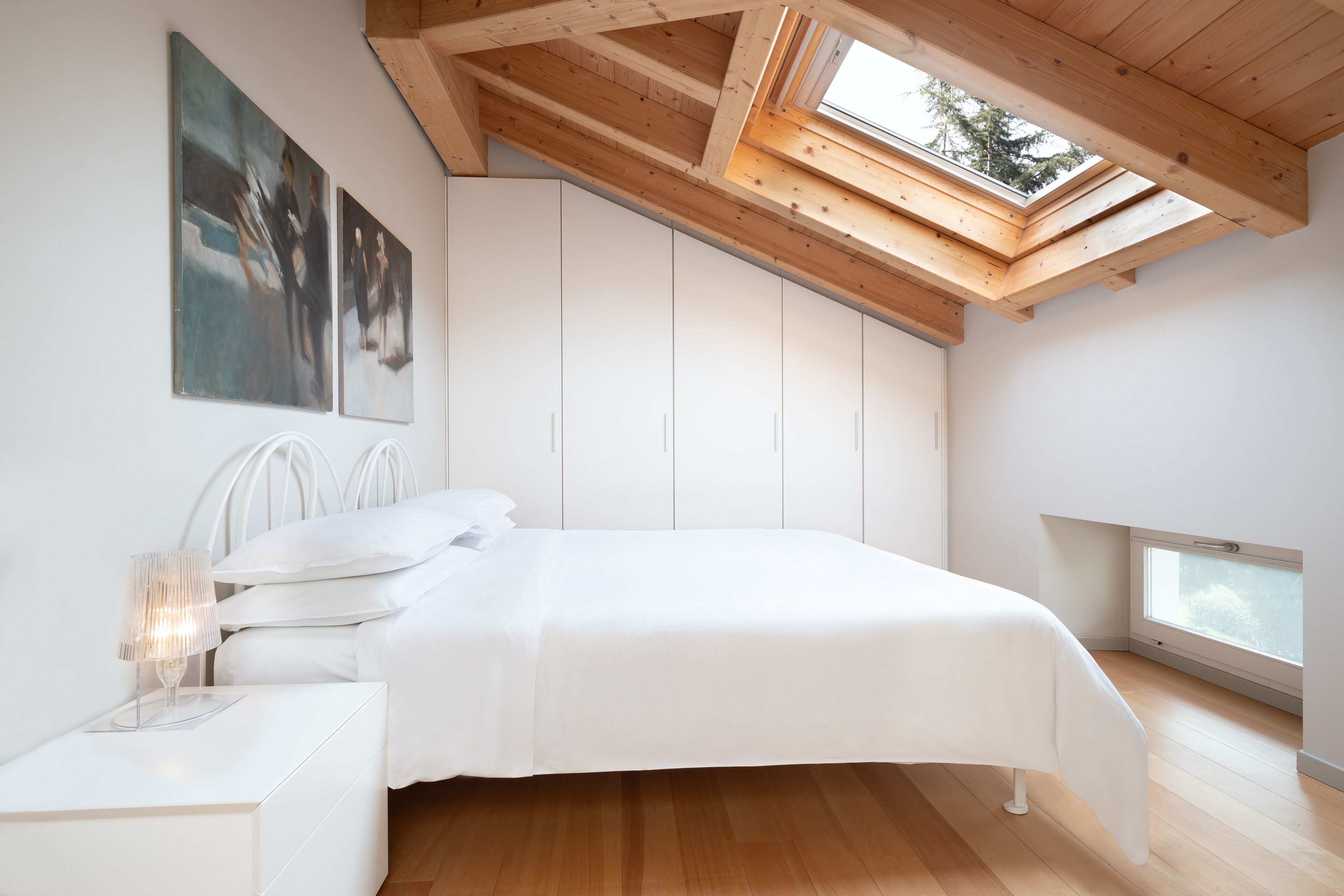 Un dormitorio con tragaluces, una cama, una mesita de noche y una obra de arte en la pared.