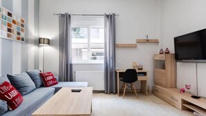 Ein modernes Wohnzimmer mit grauem Sofa, einem Holztisch, einem Schreibtisch und einem Fernseher.