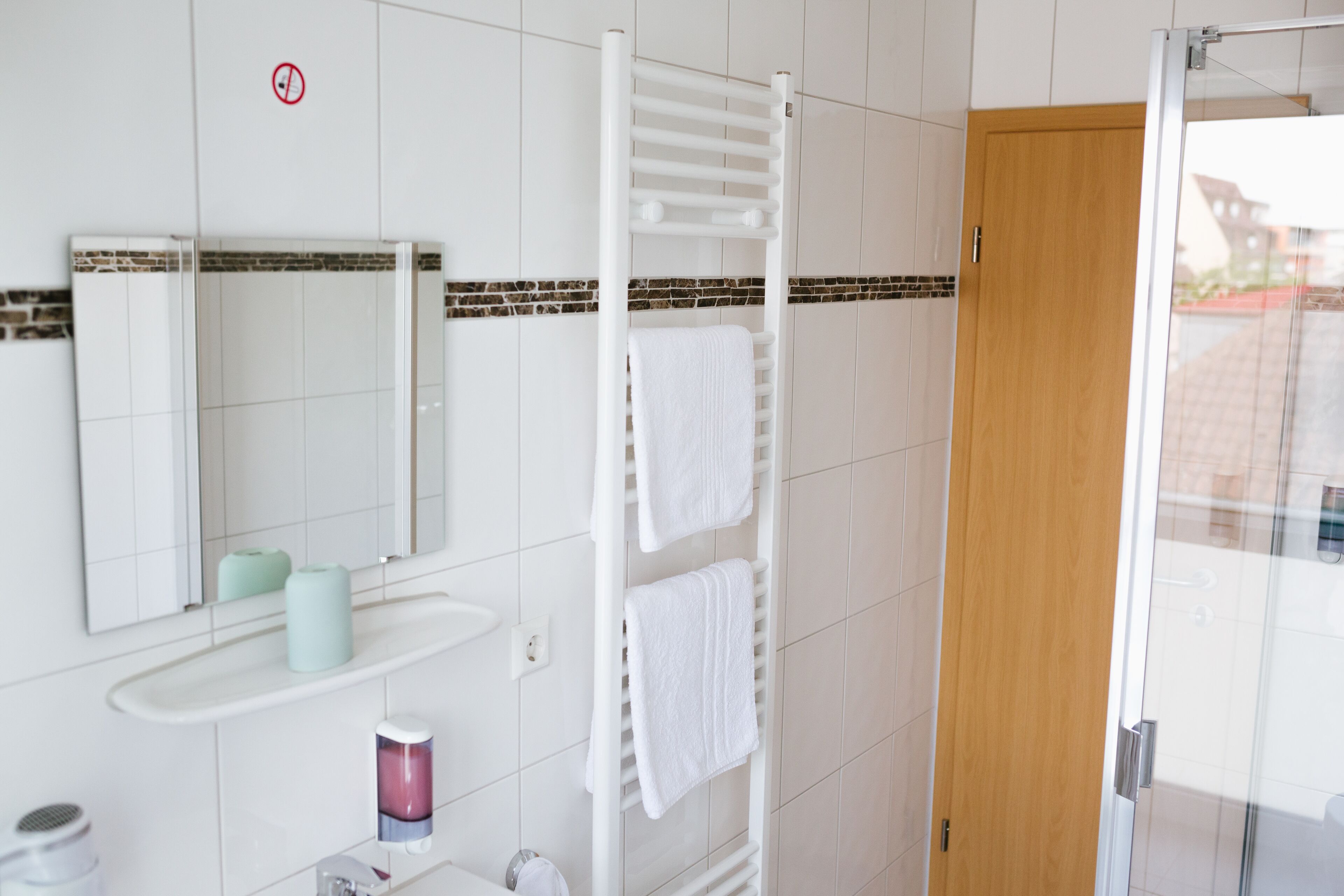 Ein Badezimmer mit weißem Handtuchhalter, einem Spiegel, einem Waschbecken und einer Duschkabine.
