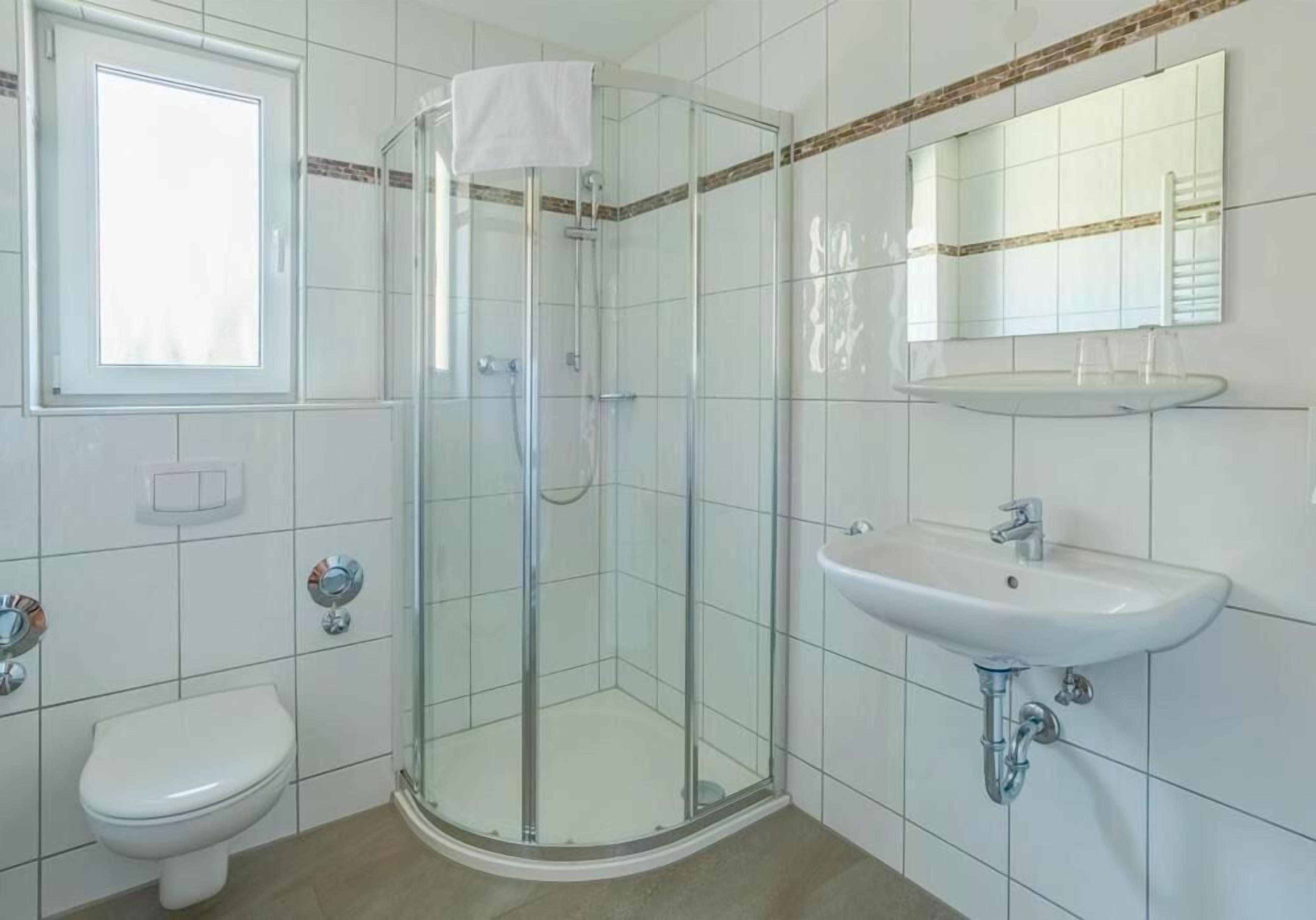 A bathroom with a glass-enclosed shower, a white sink, and a toilet.