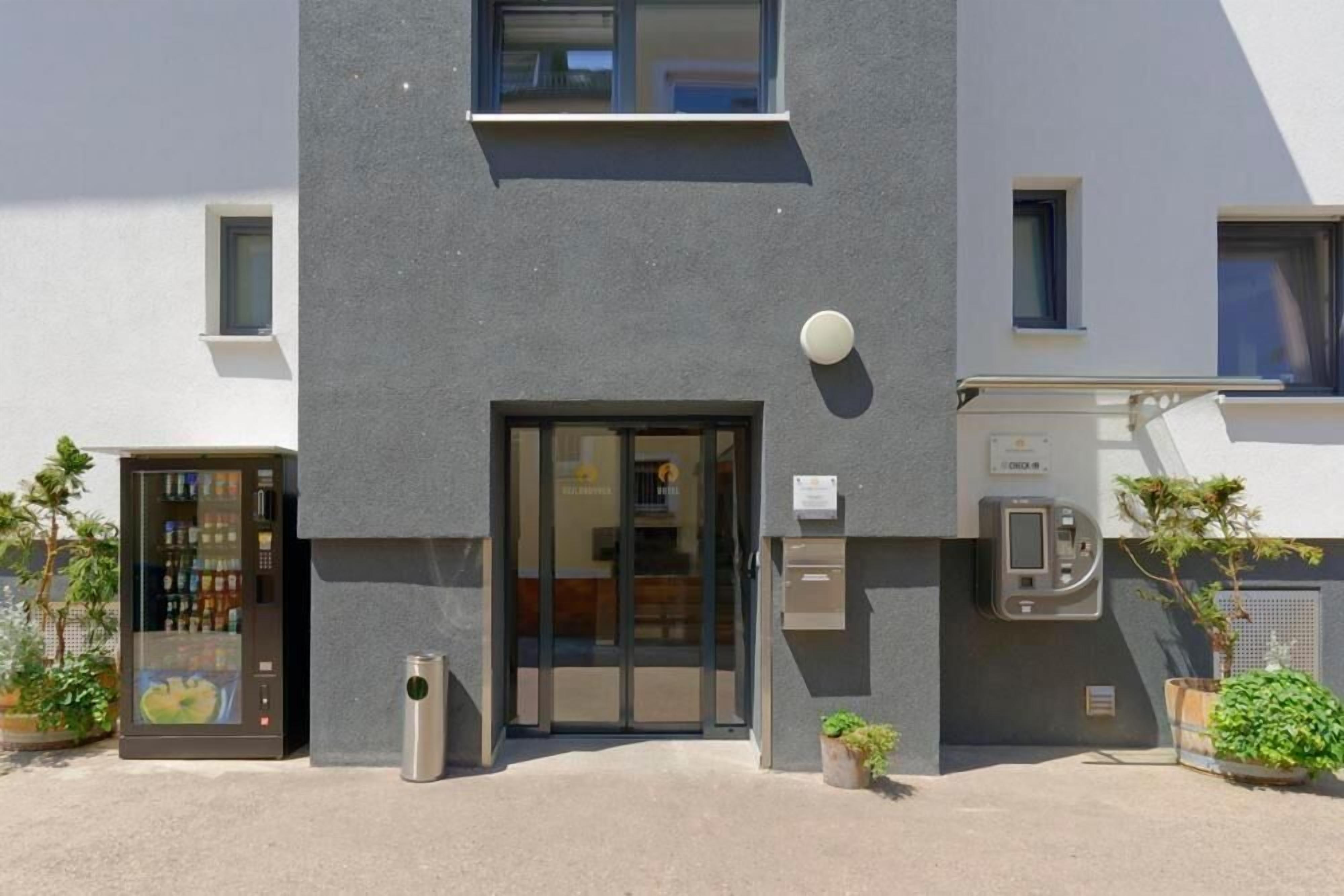 A modern building with a grey facade, a glass door entrance, a vending machine, and a small trash bin.