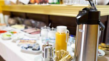 A buffet setup with various food items, a coffee maker, and a thermos.