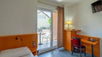 Une chambre d’hôtel comprenant un lit, un bureau avec une chaise, une lampe et donnant sur le balcon extérieur.