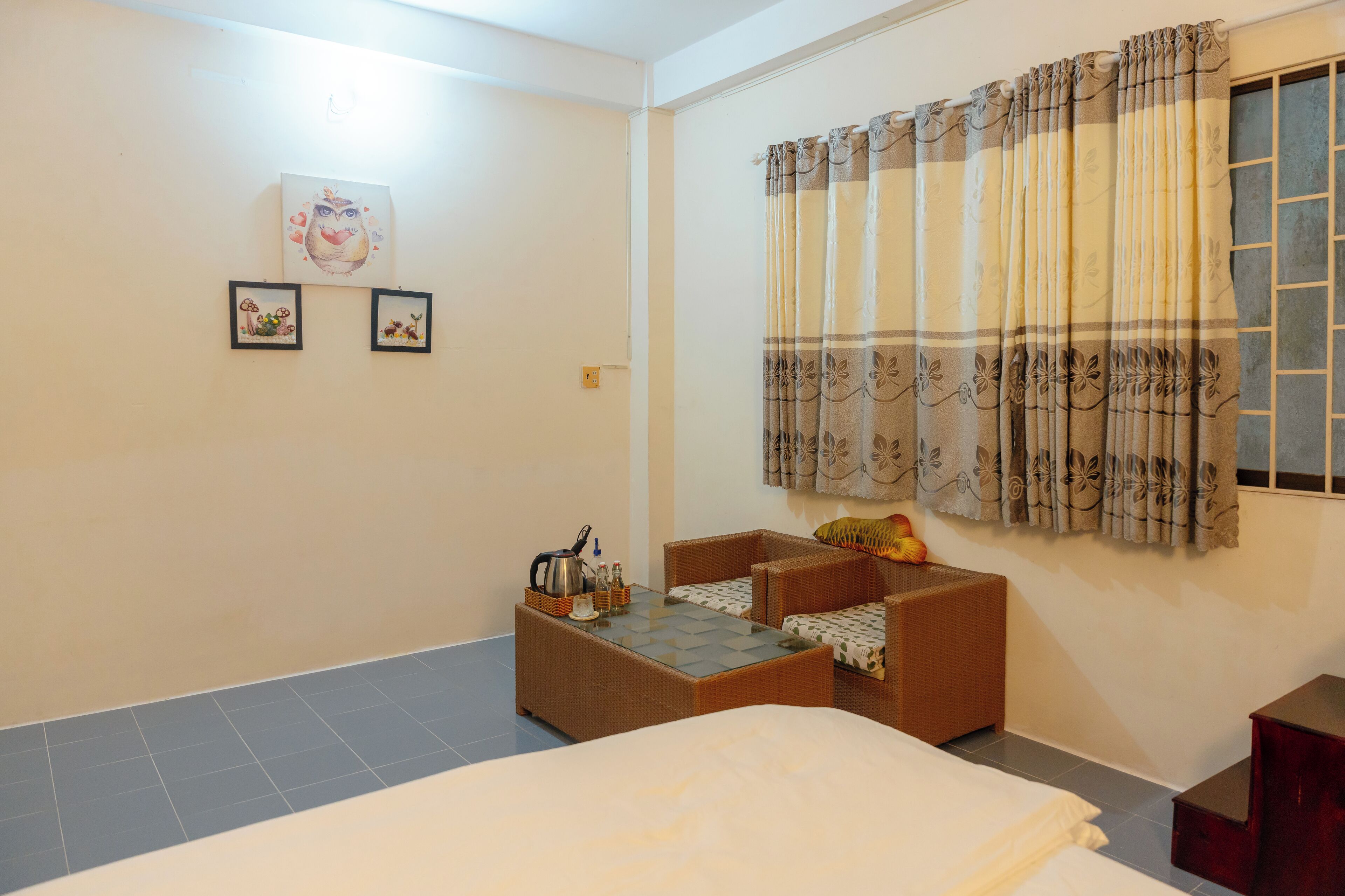 A hotel room with a bed, a small sofa, a table with a kettle, and a window with curtains.