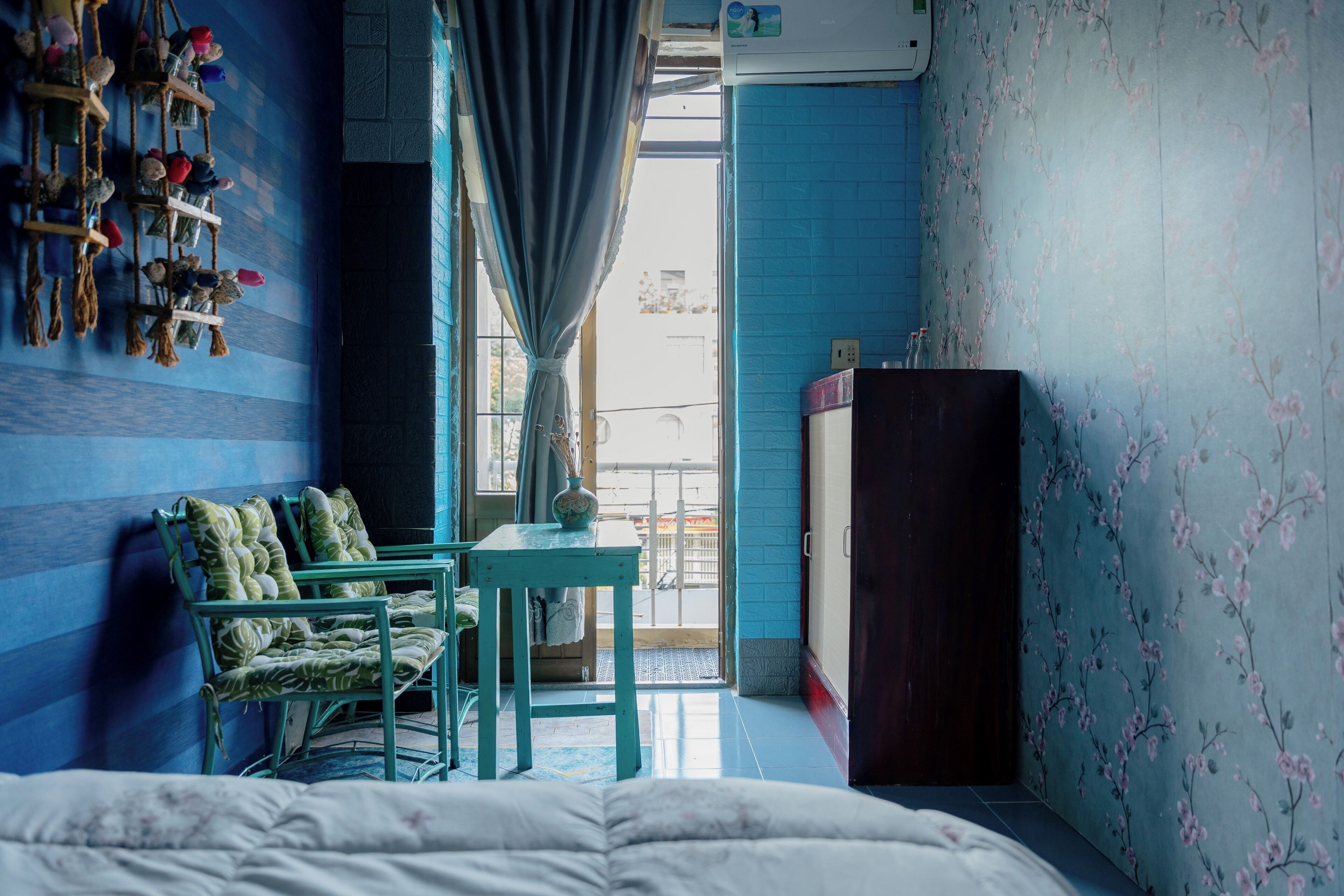 A room with a bed, a table with a vase, chairs, a wardrobe, and a window with curtains.