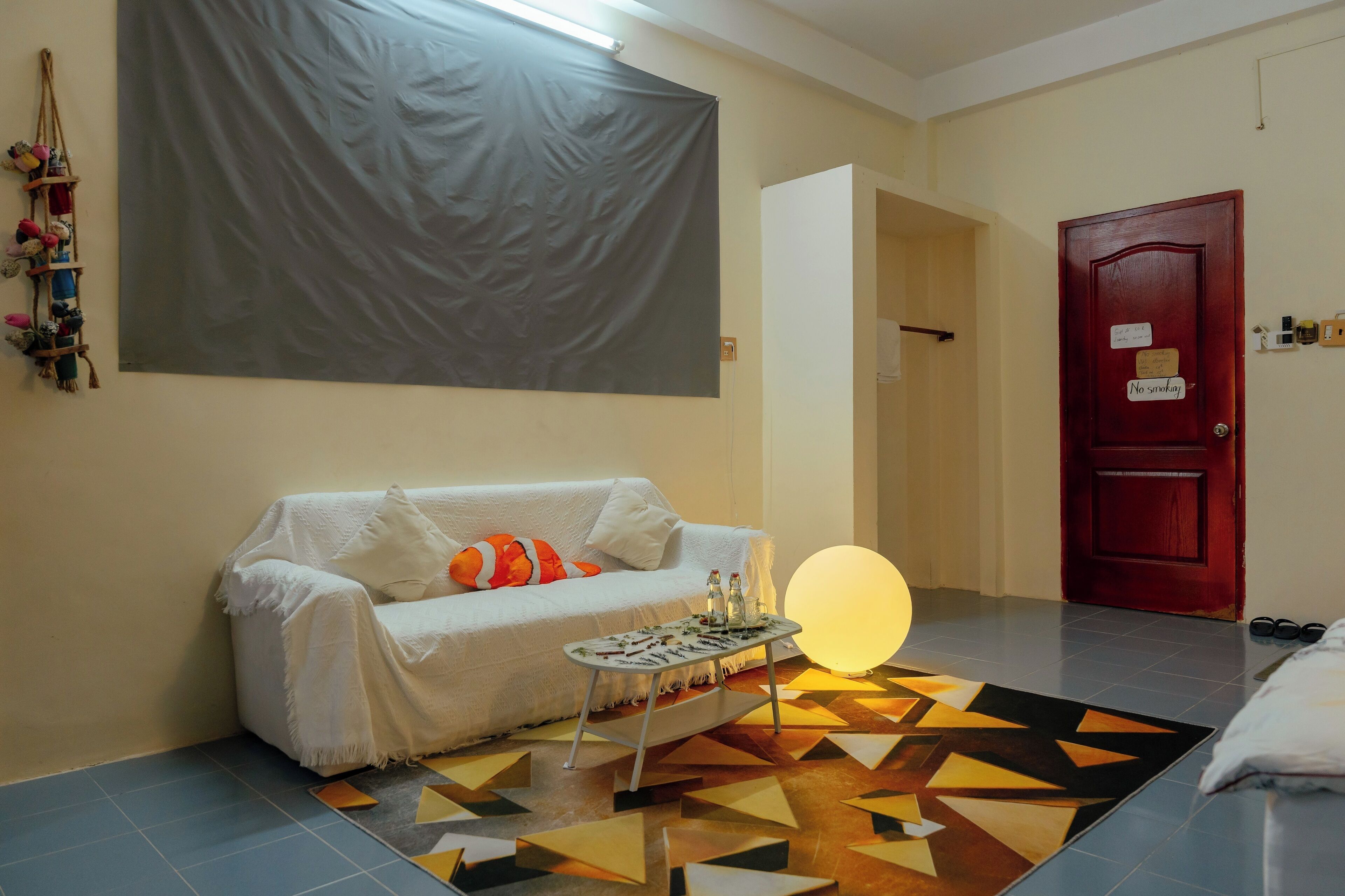 Una habitación con un sofá blanco, una mesita con objetos decorativos, un tapete de estampado geométrico y una lámpara redonda grande.