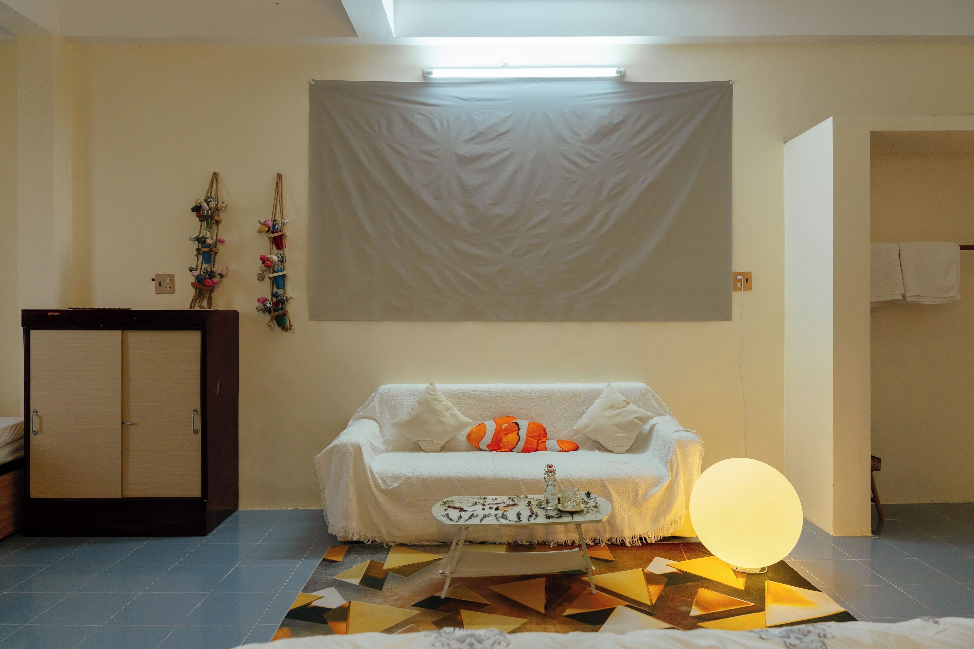 Une pièce avec un canapé blanc, une petite table, une tapisserie murale et un sol à motifs géométriques.