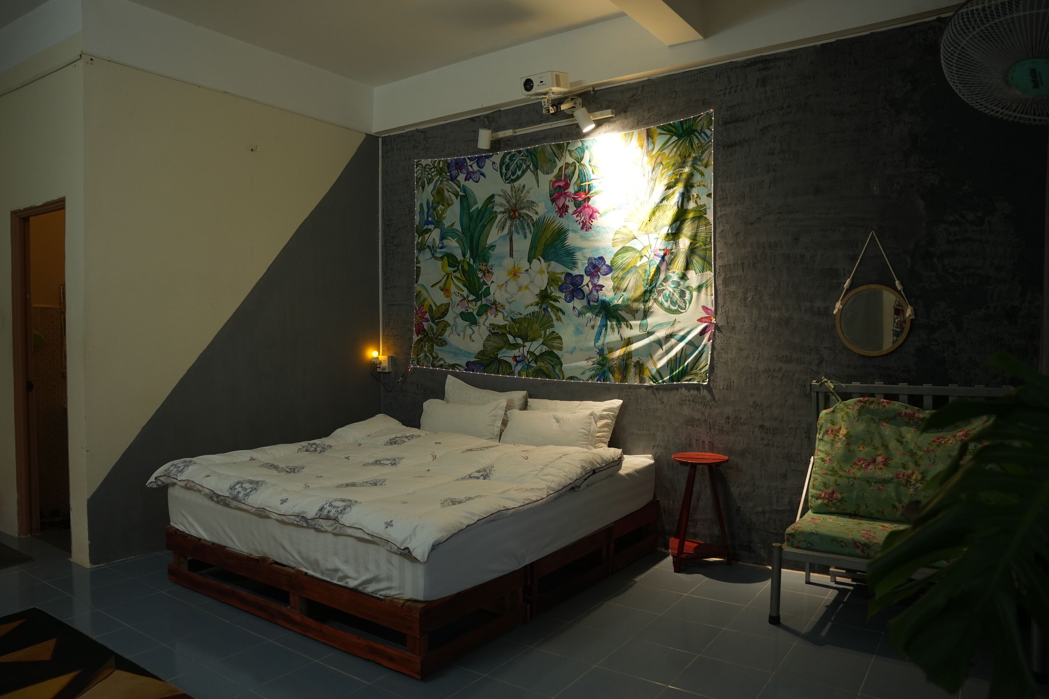 A bedroom with a bed, a wall-mounted mirror, a small table, and a chair.