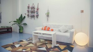 A living room with a white sofa, a coffee table, a patterned rug, a potted plant, and wall decorations. - Bui Homestay - Rach Gia Ferry Terminal (Rach Gia)