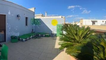 Relax on the rooftop with a table, chairs, and a bench, surrounded by a low wall and a palm tree.