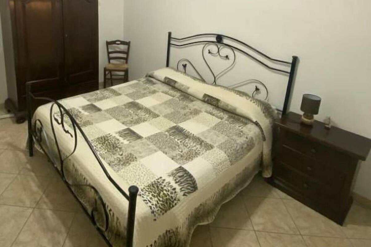 Un dormitorio con una cama, un armario de madera, una silla y una mesita de noche.