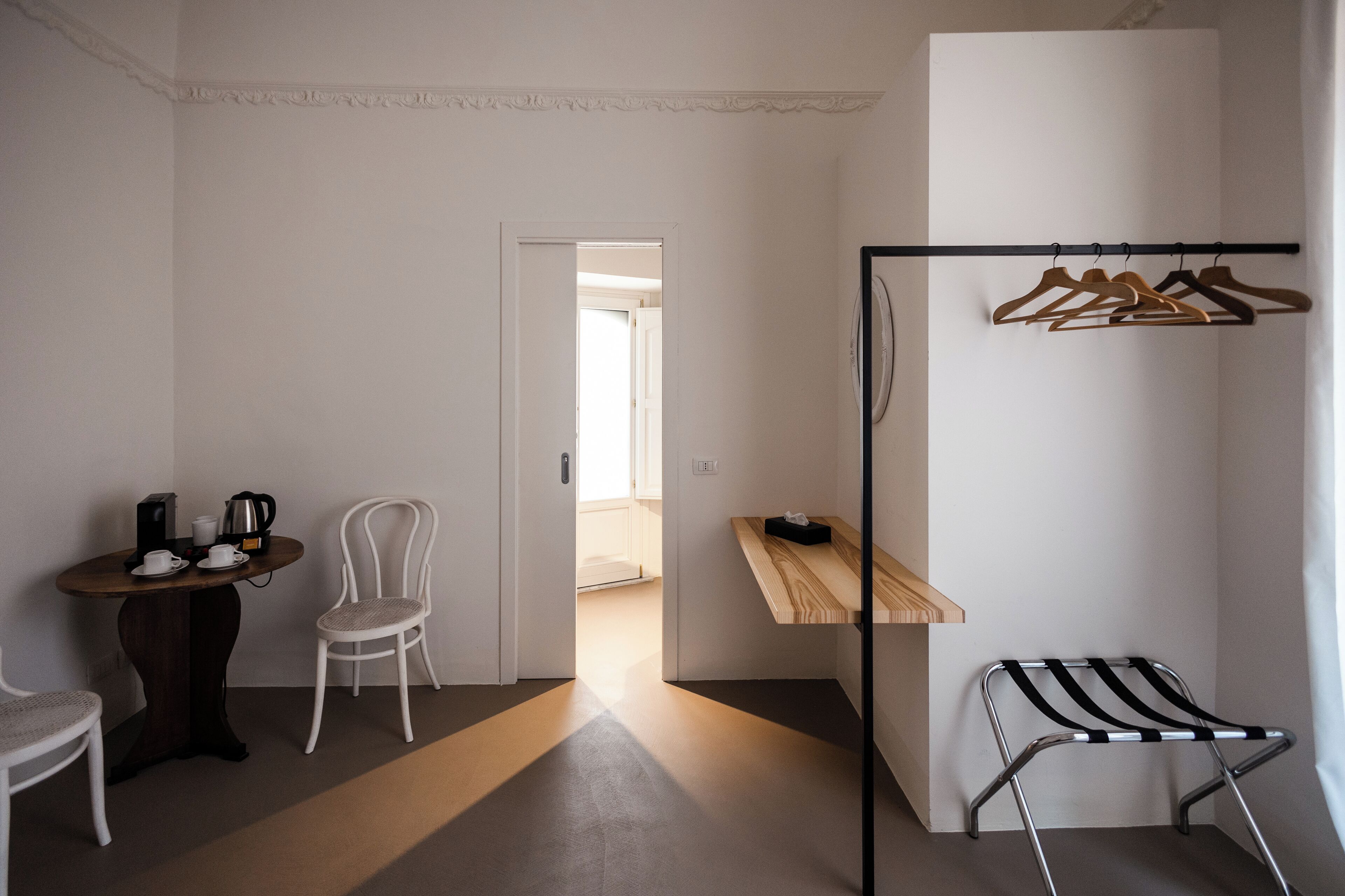 Una habitació amb taula de fusta, dues cadires, una estant per a roba penjada i un petit tamboret.